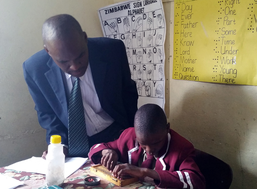 Daniel Chiomba assists Kudzai Antonyo, 9, who is learning the basics of Braille. Photo by Eveline Chikwanah, UMNS.