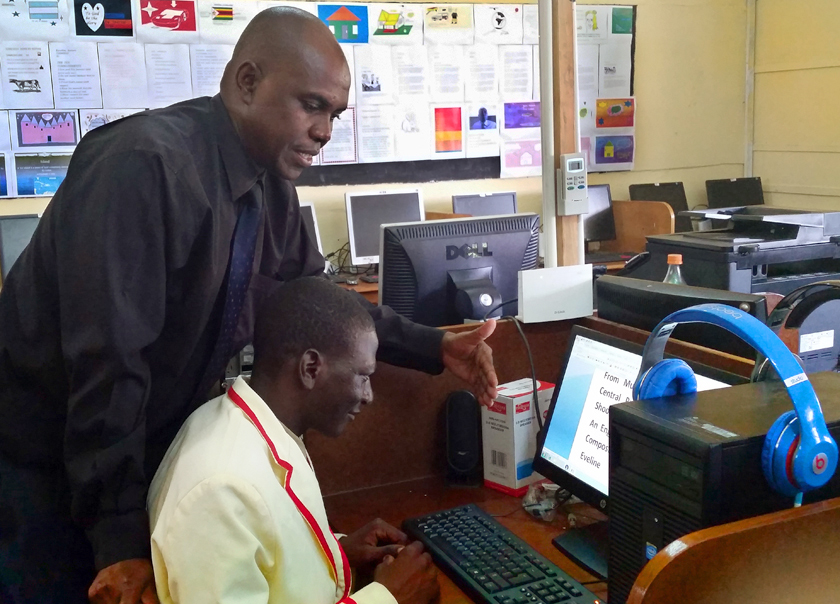 Kundayi Paradza teaches Armstrong Chiota to use a computer. Photo by Eveline Chikwanah, UMNS.