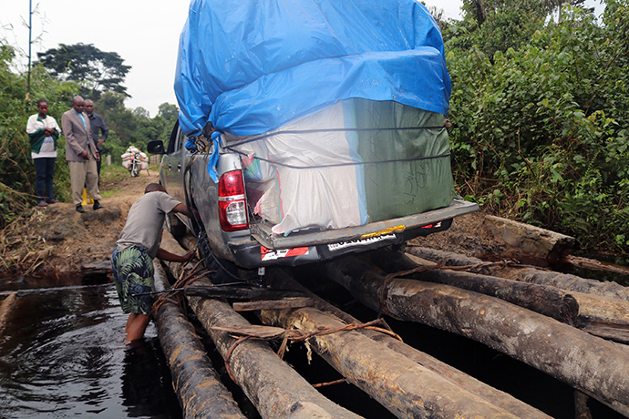 The driver of a truck bearing supplies for displaced persons in the Democratic Republic of Congo stands in water as he tries to navigate the vehicle over a rough, wooden bridge. United Methodists in the Democratic Republic of Congo have helped distribute food and other assistance in secrecy out of fear that Mai-Mai Malika rebels would take the goods. Photo by Judith Osongo Yanga, UMNS.