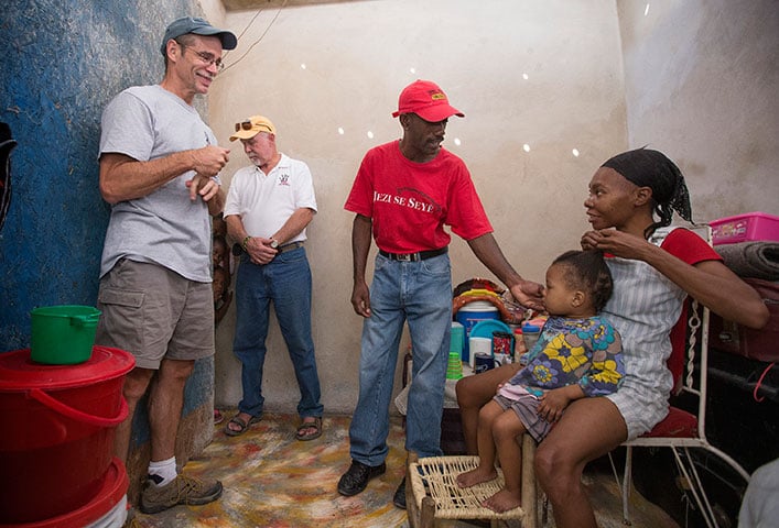 The Rev. Tom Vencuss (left) and Bill Borah visit with Jean Claude Degazon (center) in his rebuilt home. Juliet Degazon (right) and Nana, 2, are among 15 family members who live in the home. 