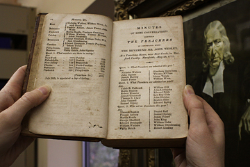 Frances Lyons-Bristol, archivist  records administrator, holds a book  listing early Methodists, just one of thousands of historic items housed at the denomination's Commission on Archives and History on the campus of Drew University in Madison, N.J. A portrait of the Rev. John Wesley hangs in the background.  A UMNS photo by Kathleen Barry.