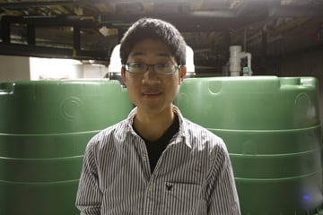 Kelvin Gu, student president of the Duke Smart Home Program, stands in front of storage tanks used to collect and distribute recycled rainwater.