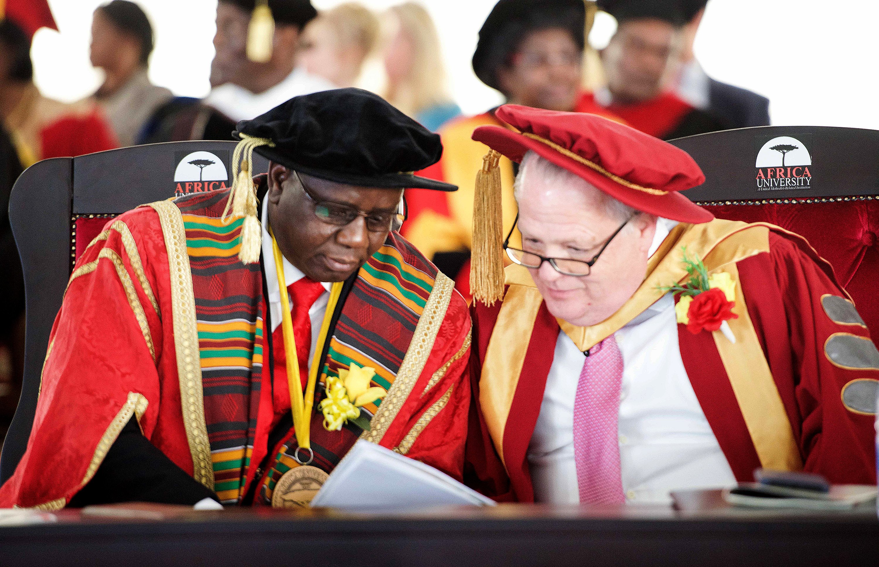 Munashe Furusa (left), vice chancellor of Africa University, confers with Timothy Keating during graduation. Keating, an executive with the Boeing Co., was guest of honor at the ceremony. His family has endowed a permanent scholarship valued at $130,000 for female students studying education. Photo by the Africa University Department of Information and Public Affairs.