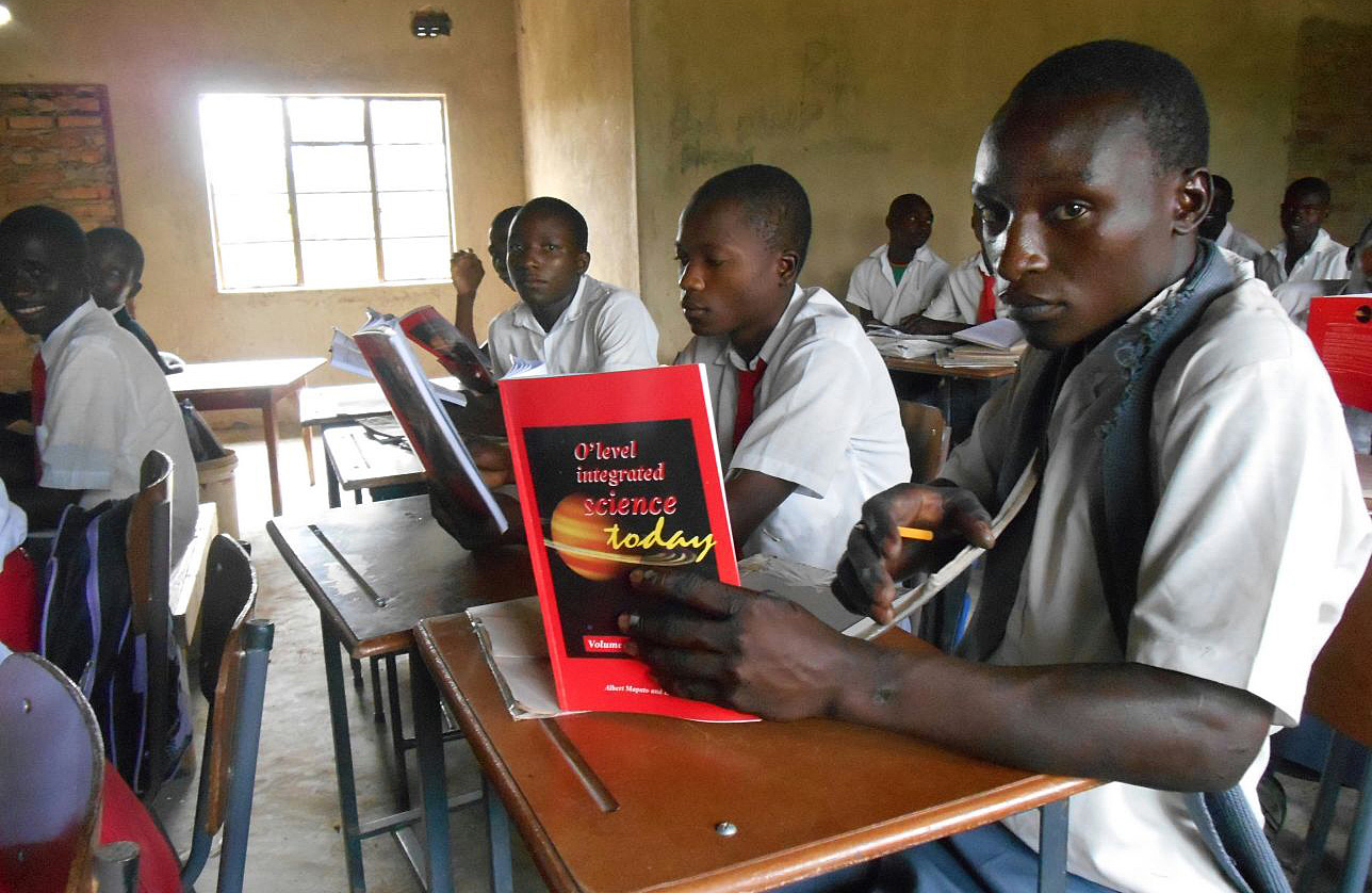 Kudzai Manyengavana, right, holds a new book donated by Stevensville (Michigan) United Methodist Church, as he attends class with other students in a temporary school building at Arnoldine Mission in 2016. Photo courtesy of Brian Mbwizhu.  