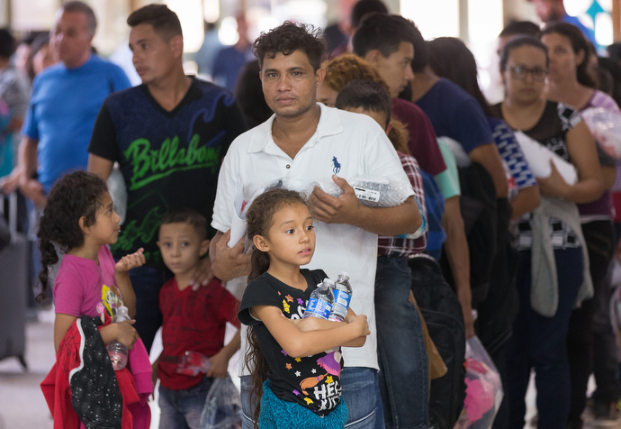 Bewildered immigrants who have just been released from a U.S. Border Patrol detention facility clutch water bottles and personal belongings while they wait in line at the bus station in McAllen, Texas. Photo by Mike DuBose, UMNS.