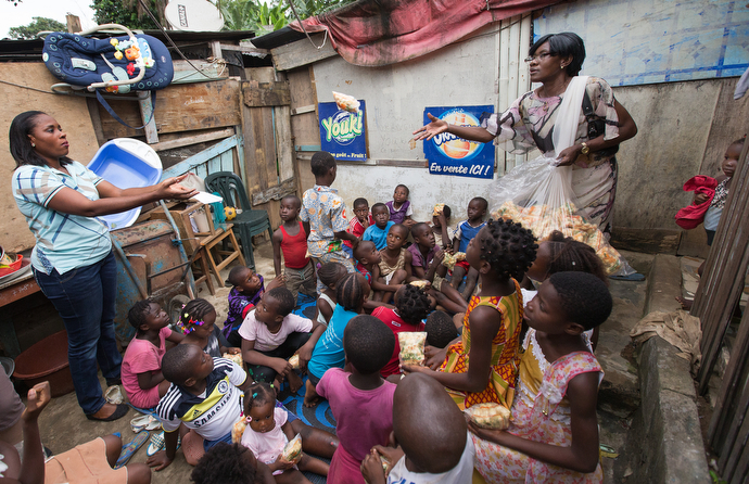 Cécile Agnies Nouie (standing, right) tosses a snack bag to fellow volunteer Estelle Kouame at New Jerusalem United Methodist Church. Photo by Mike DuBose, UMNS.