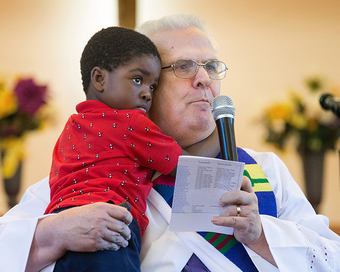 The Rev. Bill Jenkins, gives the sermon during worship at Exodus United Methodist Church in San Diego while holding his foster son Harry, who is from Haiti. The church is the only immigrant-welcoming center in Southern California. Photo by Mike DuBose, UMNS.