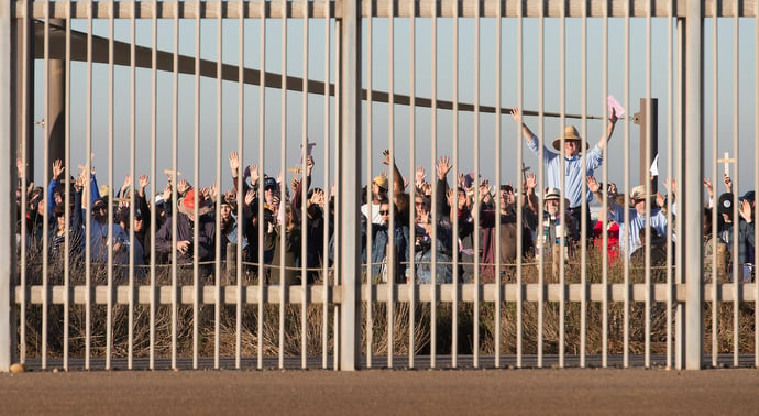 United Methodist pastor John Fanestil (standing above crowd at right) leads participants in a Posada celebration on the U.S. side of a secondary border fence that separates San Diego from Tijuana, Mexico. On the 25th anniversary of La Posada Without Borders, Friendship Park was closed on the U.S. side while hundreds gathered freely on the Mexico side. 