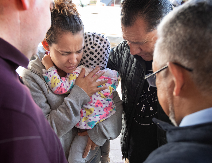 The Rev. Arturo Gonzélez Sandouzl (second from right) and other members of the United Methodist Immigration Task Force pray with Isabél and her 16-month-old daughter Kassandra at a makeshift camp near the bridge leading to the U.S. in Matamoros, Mexico. The mother and daughter traveled from Nicaragua in hopes of seeking asylum in the U.S. Photo by Mike DuBose, UMNS.