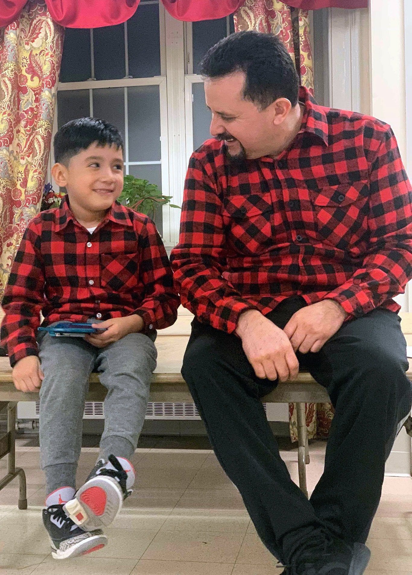 Nelson Pinos sits with his son, Brandon Pinos, age 6, in the fellowship hall of First and Summerfield United Methodist Church in New Haven, Conn. Pinos, who has lived in the U.S. for 26 years, is currently living in sanctuary at the church. Image courtesy of the "Keep Nelson Home" Facebook page.