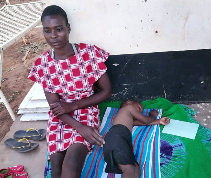 Martha Banda, 26, and daughter Priority Chimombe wait to go back home to Chaparapata Village after the 3-year-old was treated for malaria at Dindi United Methodist Clinic in the Murehwa Uzumba Maramba Pfungwe District in Zimbabwe. The clinic has been overwhelmed by an outbreak of malaria in the area. Photo by Kudzai Chingwe, UM News.