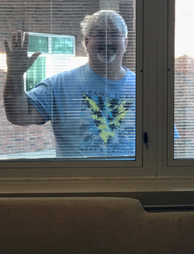 The Rev. Kim Strong, pastor of Trinity United Methodist Church in Conway, S.C., waves through the blinds at his wife, Margo, who was hospitalized in March with COVID-19. She took the photo during one of his window visits. Margo Strong has since recovered. Photo courtesy of Kim and Margo Strong.