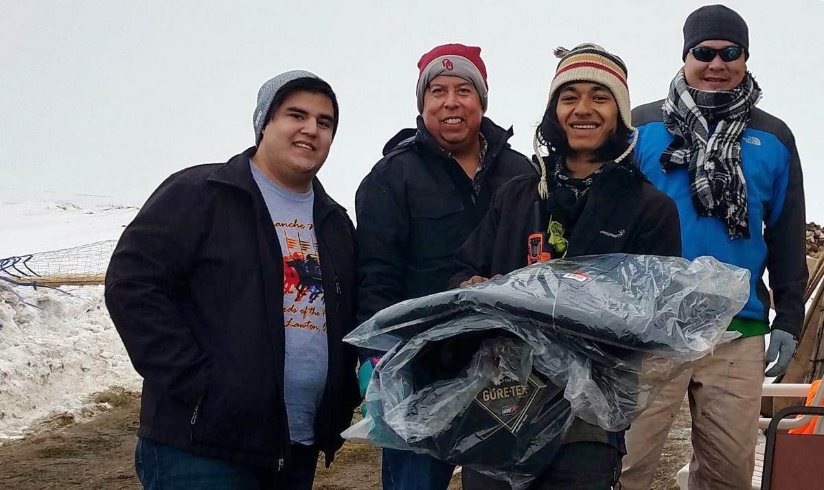 Dallas Parker, left, the Rev. David Wilson, second from left, and Tim Byington, right, present thermal coats to a camp volunteer at the Oceti Sakawin Camp at Standing Rock in Cannon Ball, N.D. in this 2017 file photo. The coats were donated by the Urban Inter-Tribal Center of Texas. File photo courtesy of Dallas Parker.