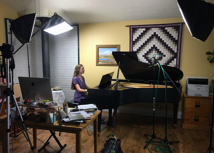 Freya Wardlaw-Bailey, accompanist for St. John United Methodist Church in Anchorage, Alaska, plays the piano amid equipment used for making virtual choir videos. Her husband, James Wardlaw-Bailey, leads the church’s choir program and does the video editing, spending three or four hours per anthem. Photo courtesy of James Wardlaw-Bailey.