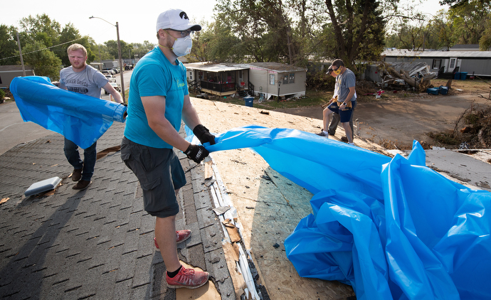 The Rev. Simon Campbell (center foreground) helps spread a plastic tarp over the roof of a storm-damaged home in Marion, Iowa. Campbell was leading a volunteer team from Marion Cares, a ministry of Marion First United Methodist Church. Volunteer Tyler Hungate is at left. Photo by Mike DuBose, UM News.