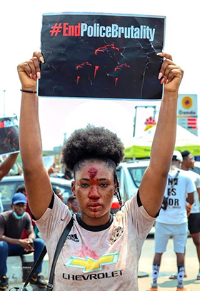 A woman — wearing makeup to look like blood in protest of police brutality — holds a sign at the Lekki toll gate in Lagos, Nigeria. Demonstrations there turned deadly on Oct. 20. Photo by the Rev. Ande Emmanuel, UM News