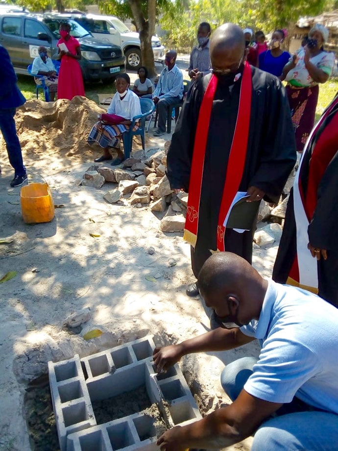 O Construtor preparando o terreno para lançamento da pedra em Dondo, Moçambique. No fundo vê-se os membros daquela comunidade sentados. Foto de Eurico Gustavo.