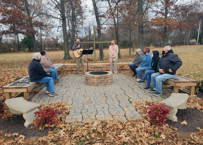 Volunteers from the food pantry at Benton First United Methodist Church in Benton, Ky., gather around the fire pit on the church property for “yard worship.” The Rev. Leah Howe and Worship Director Scott Gibbs are providing outdoor services at the homes of people who do not feel comfortable gathering in large groups. Photo courtesy of Benton First United Methodist Church.