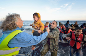 Volunteers carry a child ashore on a beach near Molyvos, on the Greek island of Lesbos, on Oct. 30, 2015, after a group of refugees crossed the Aegean Sea from Turkey in a small overcrowded boat provided by Turkish traffickers to whom the refugees paid huge sums. The refugees were received in Greece by local and international volunteers, then proceeded on their way toward western Europe. File photo by Paul Jeffrey/Life on Earth Pictures.