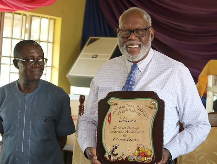 Bishop Warner Brown holds a plaque given to him by staff of the Bishop Jane Middleton High School in Freetown when he toured the facility. Photo by Phileas Jusu, UM News.