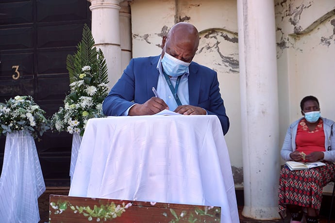 Micheal Dengwani writes a message of condolence during the outdoor funeral of Lillian Chikomo in Harare, Zimbabwe. Photo by Kudzai Chingwe, UM News.