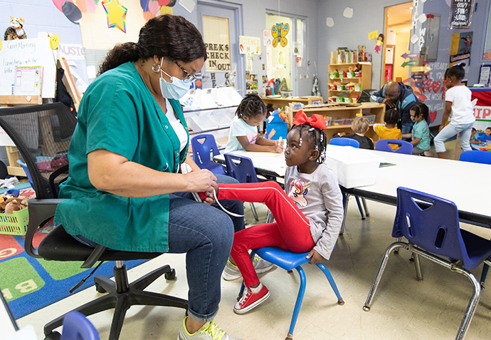 Teacher Karen Coure helps daycare student Melody with her shoes at Bethlehem Centers. Photo by Mike DuBose, UM News.