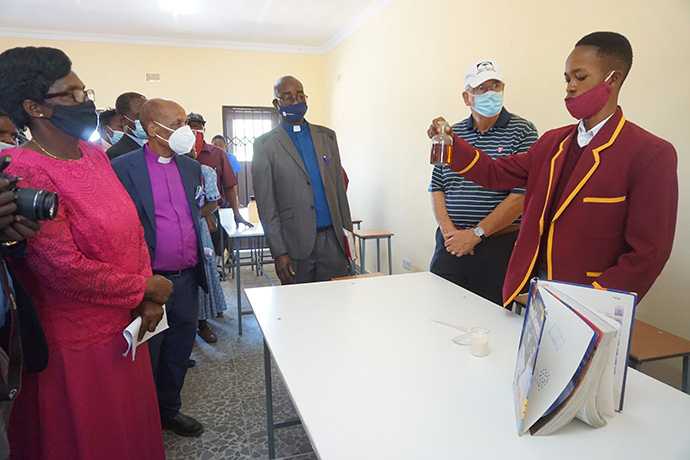 Student Ashley Bhaudhi demonstrates a science experiment for church leaders including Zimbabwe Area Bishop Eben K. Nhiwatiwa (in purple shirt) and Charles Eric Moore Jr., leader of the Zimbabwe Volunteers in Mission team that provided funds for the new laboratory. Photo by Kudzai Chingwe, UM News.