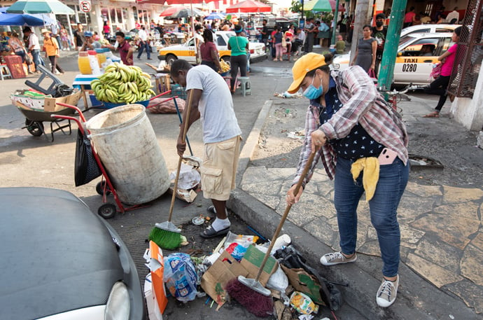 Leticia (right), from Honduras, and Felipé, from Haiti, clean trash from the gutters in Tapachula. The municipal government pays a small stipend to migrants in exchange for their work. Photo by Mike DuBose, UM News.