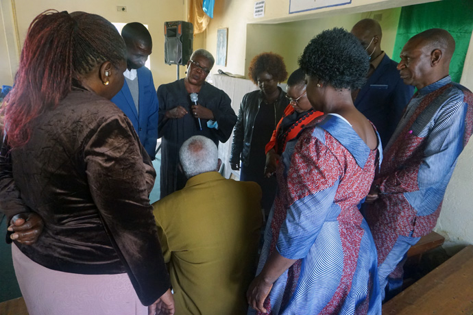 The Rev Faith Nyagato (center, with microphone), St. Peters Seke North United Methodist Church associate pastor, offers encouragement to Toendepi Samson Marikasi (center, with back to camera) as other pastors wait to pray with him during a special memorial service at St. James Hwedza United Methodist Church in Zimbabwe. Photo by Kudzai Chingwe, UM News.