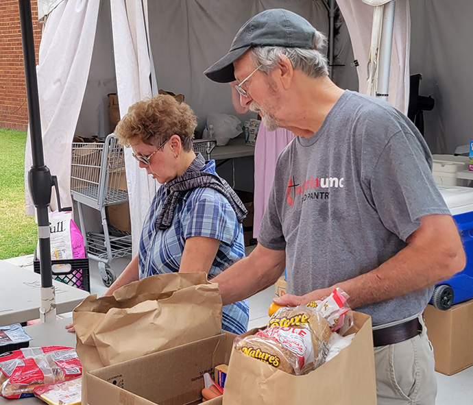 Volunteers Marcia Garst and Joe Campbell bag groceries in 100-degree heat for McFarlin Memorial United Methodist Church’s drive-thru food pantry in Norman, Okla. Photo by Scott Meier.